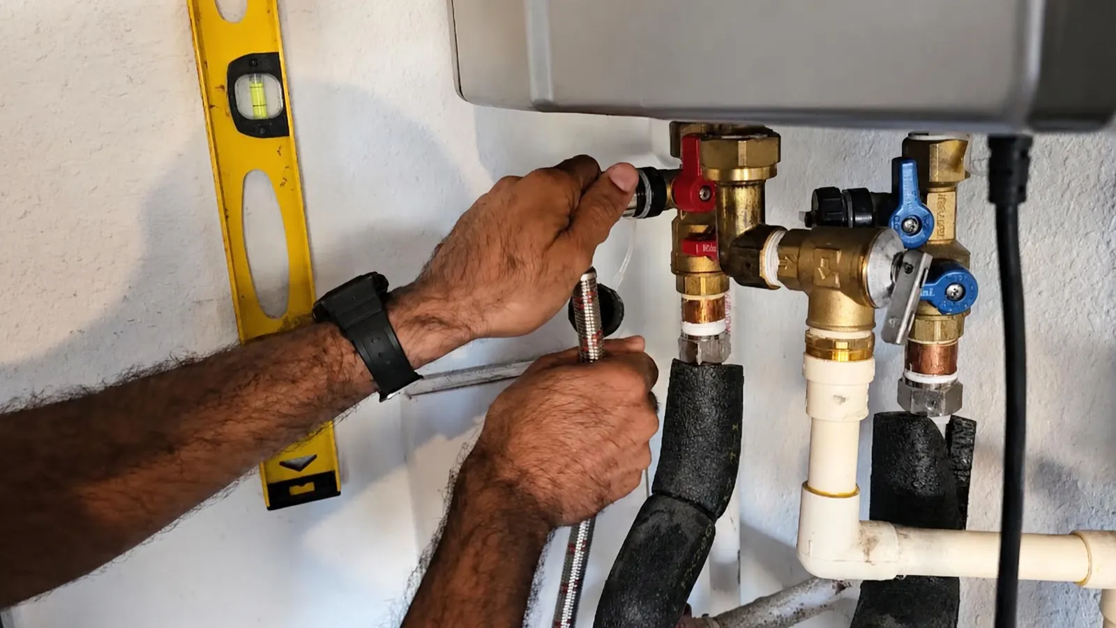 Plumber connecting isolation valves and a level to a wall-mounted tankless water heater